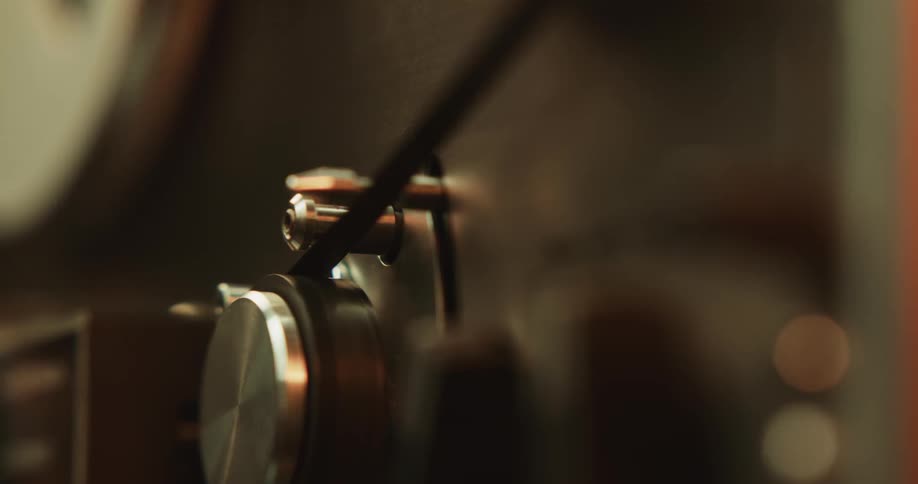 A person reaches over and pushes a button on a reel to reel tape player with their finger