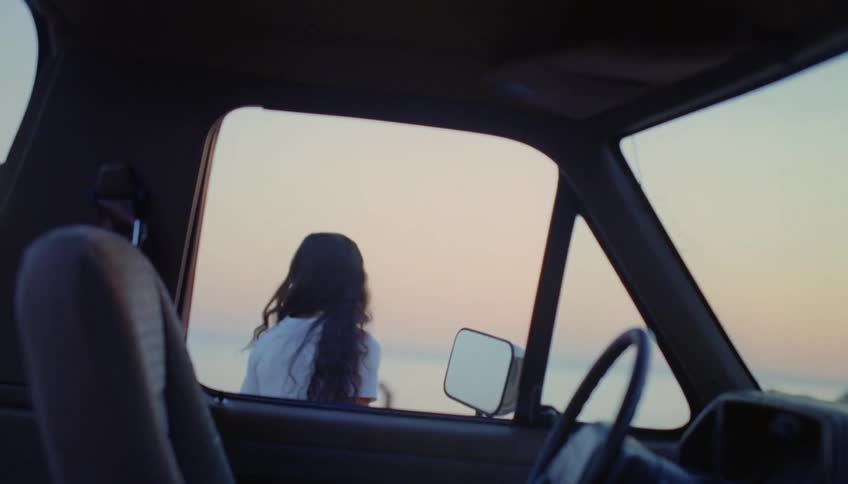 Young woman gets out of a parked car to look at the horizon at evening