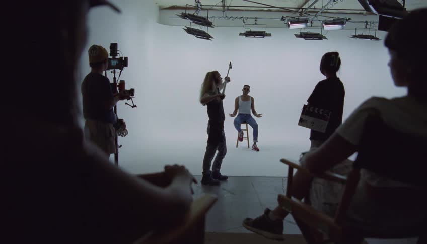 A film production is in action as a man sits on a stool