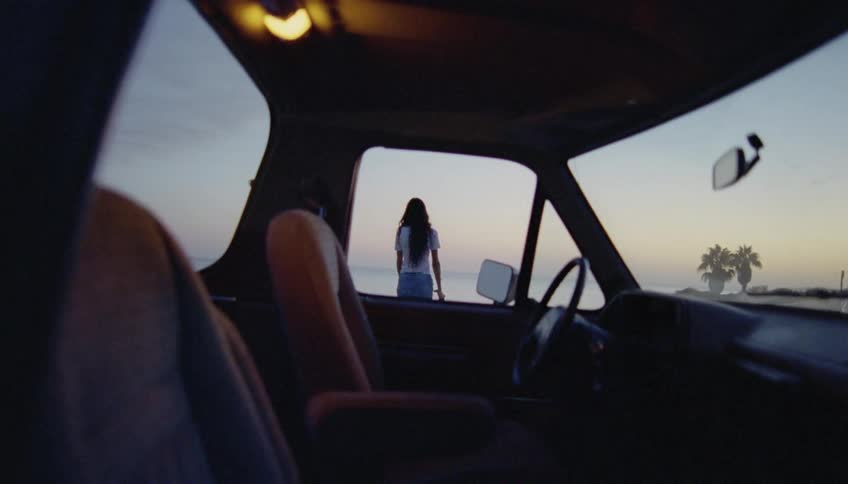 A woman parks her truck and gets out and walks towards the shore and looks at the water