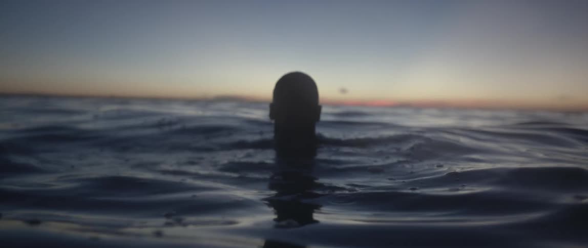 A person emerges from the ocean at dusk