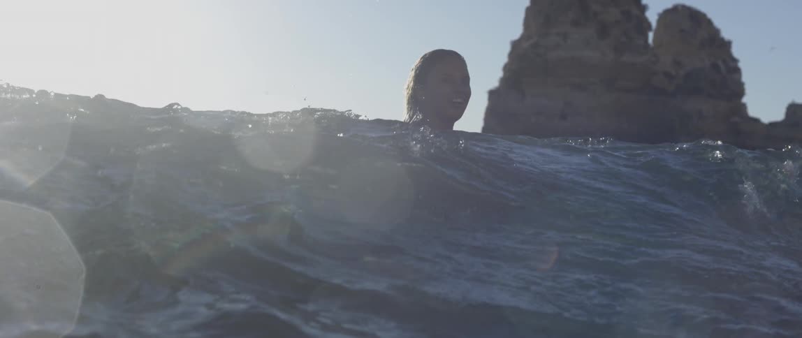 Person swimming near large rocks in the ocean