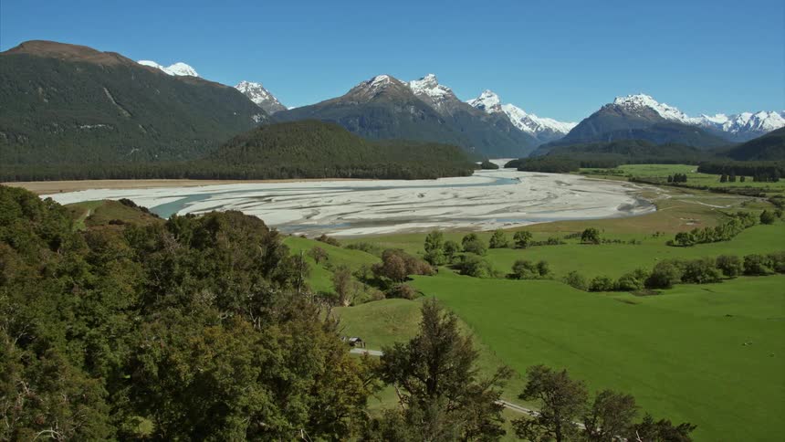 Wide aerial view of mountains and river in the distance flying over mature treetops