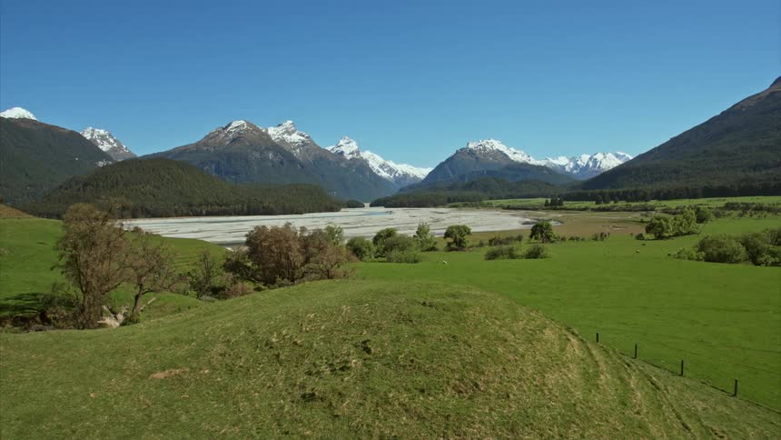 Boom up from green grass covered hill to reveal mountain landscape view