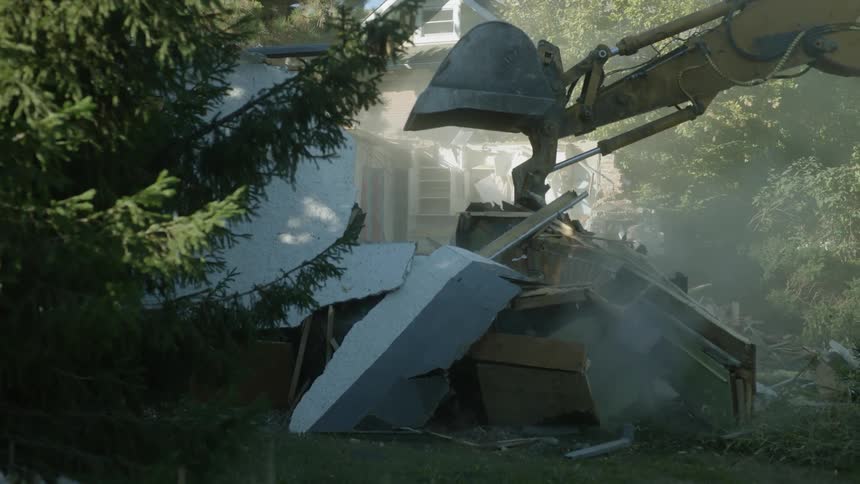 A bulldozer strikes the roof of a home
