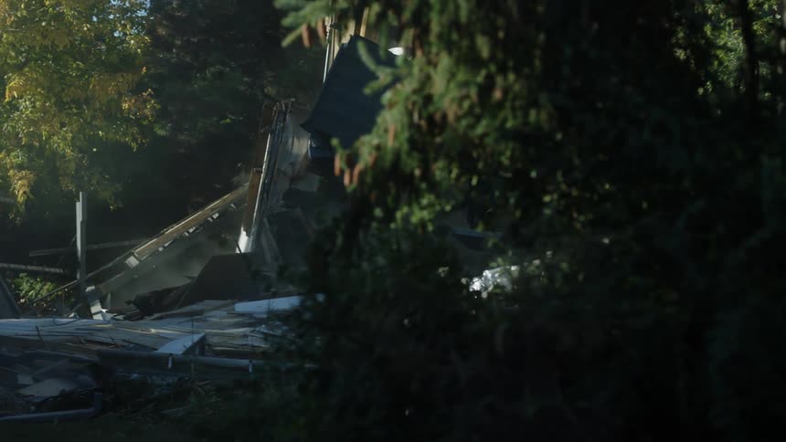 A bulldozer razes a home along a hilly neighborhood