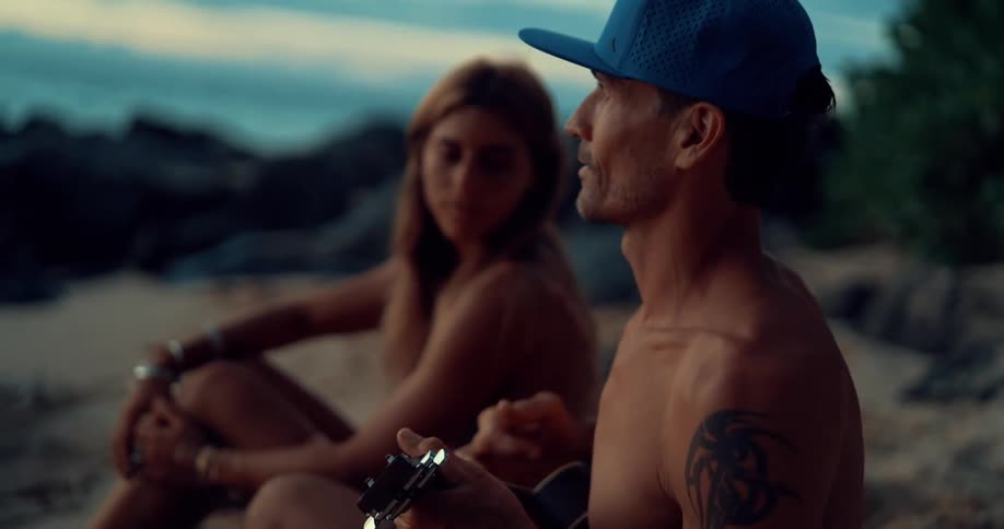A man strums a ukulele on the beach next to a woman