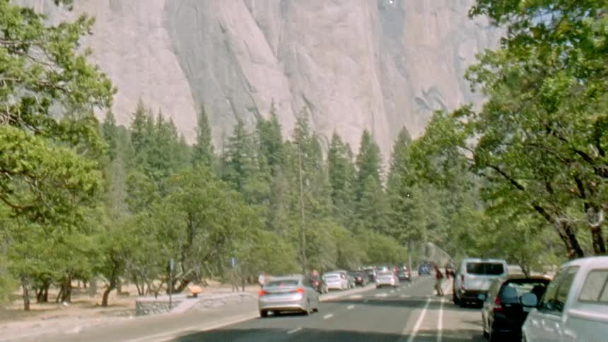 Cars are driving on a road next to a mountain