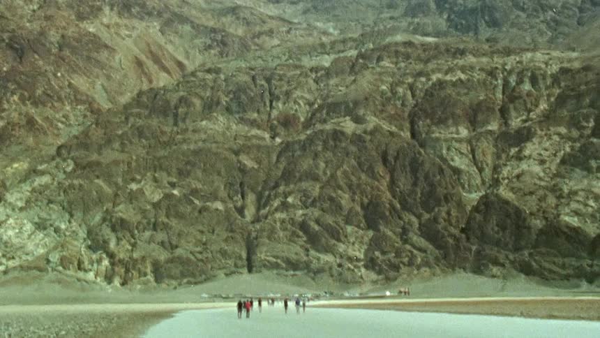 People walking on the shore and in a lake by a mountain