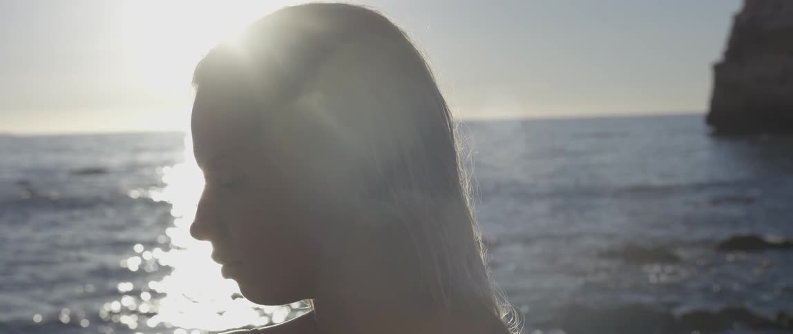 A woman stands beside the water in the sunlight