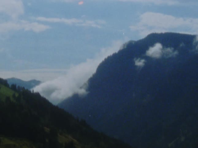 Clouds over top of tree covered hills
