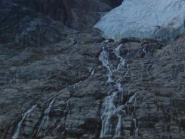 Waterfalls flowing over a cliffside into an icy body of water