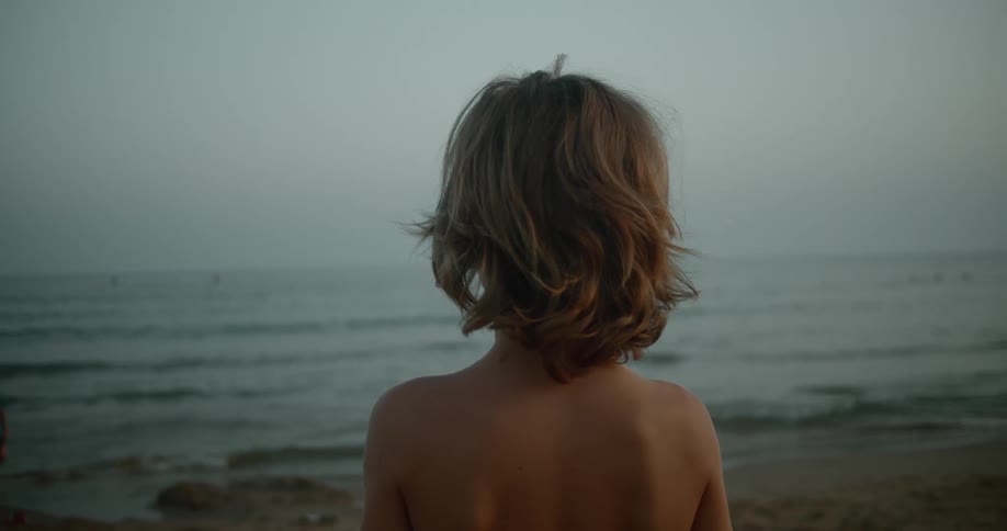 A boy is standing on the beach watching the waves roll into shore