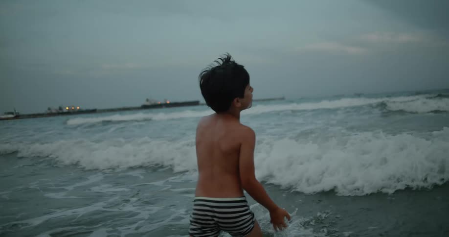 A young kid is walking in the ocean in the day time