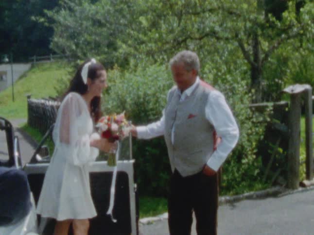 Gray haired father meets daughter dressed as bride as she exits car