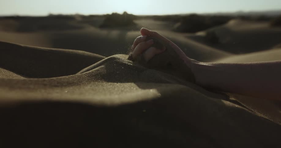 A man runs his hand through sand on the beach