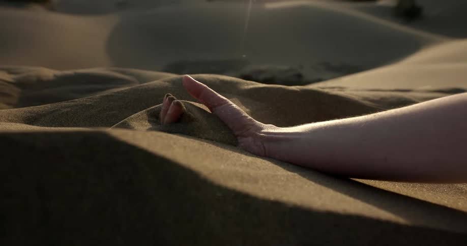 Close up of the hand of a person picking up sand from a dune in the desert at morning