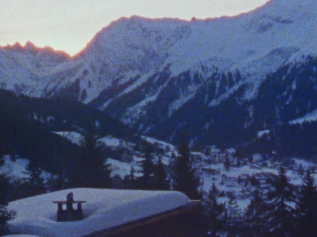 A snow covered cabin in mountains at sunset