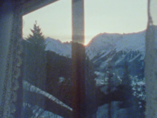 A man opens his curtains to look at snow capped mountains outside