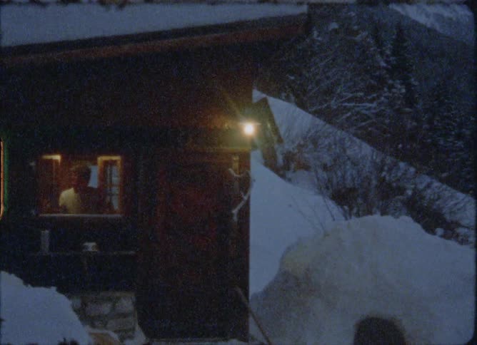 Man opens the window of a small wooden cabin on the snow covered mountains at morning caught on vintage film