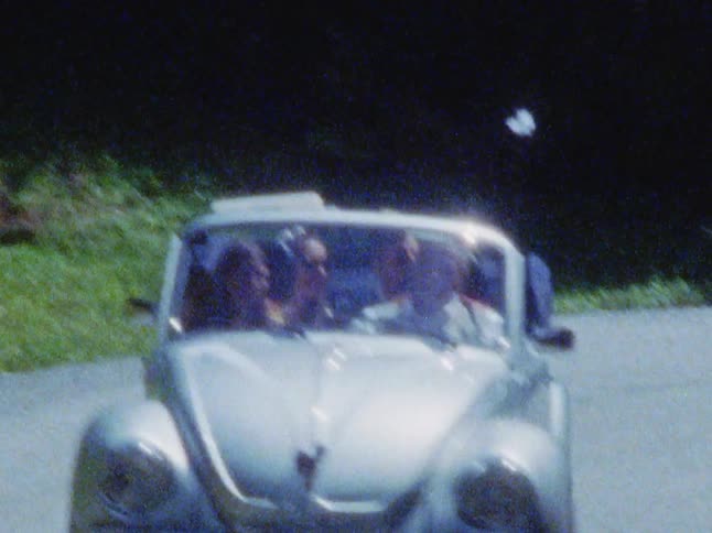 A couple drive down a curved road in a convertible