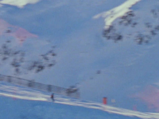A person slides down on skis down the snow covered slope of a mountain caught on vintage film
