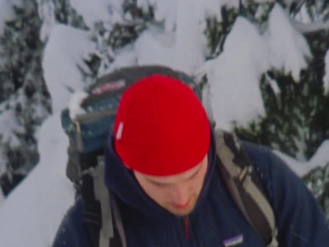 A man hiking through snowy trees with hiking poles in winter