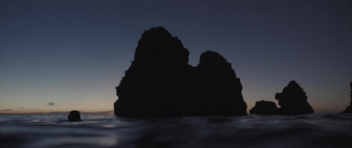 A woman treading water near large rock formations during sunset