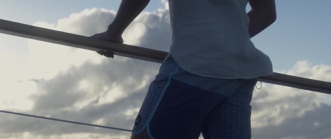 A man is standing on a boat, holding onto the rail, and watching ahead