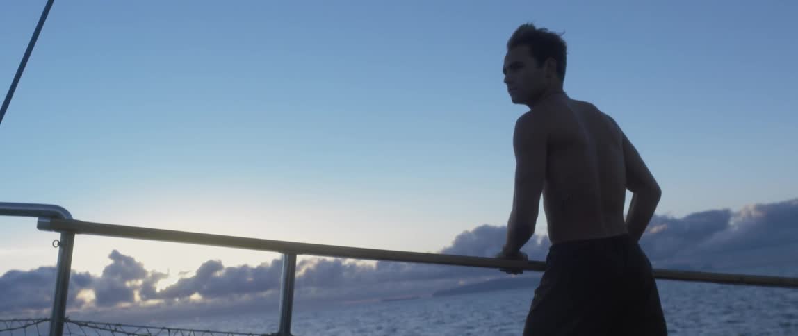 Man holding onto a rail of a ship with clouds low on the horizon