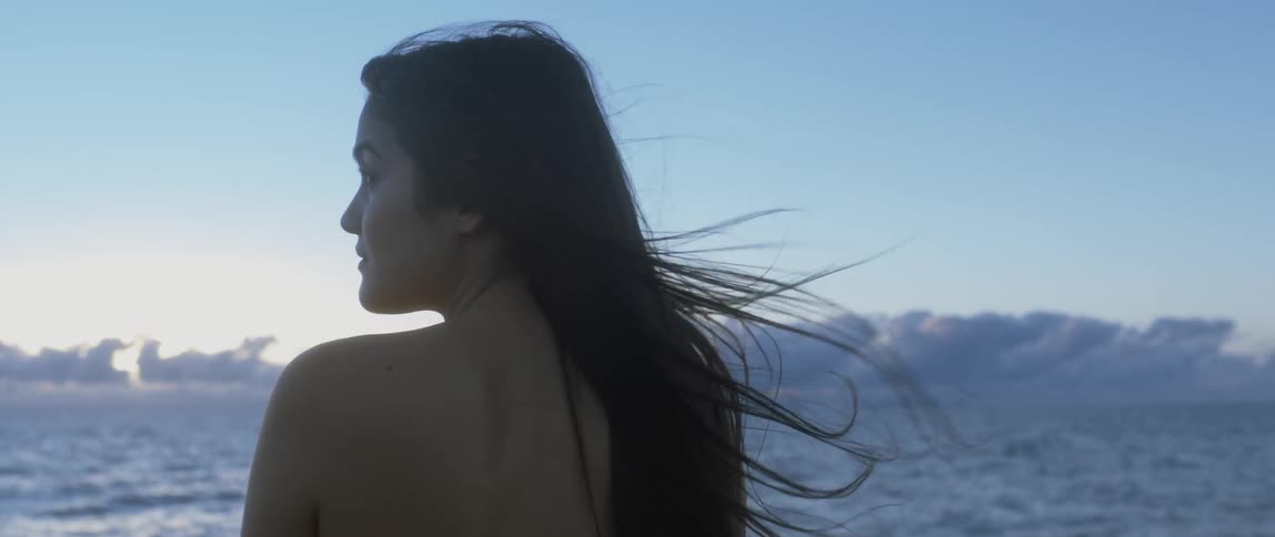 A woman stands near the ocean on a windy day
