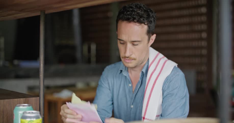 A man in a restaurant looks at receipts and then sets them on a shelf