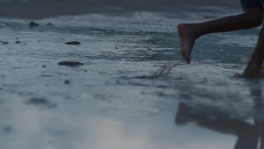 A boy is running barefoot in a puddle of water in the rain splashing as he runs