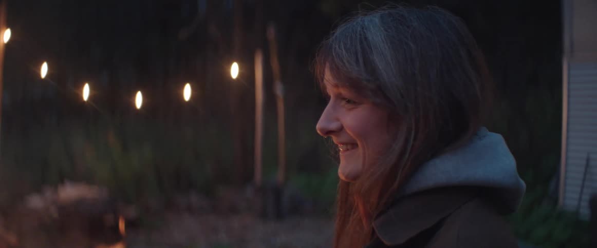 A woman is sitting outside of her house near a fire with a smile on her face