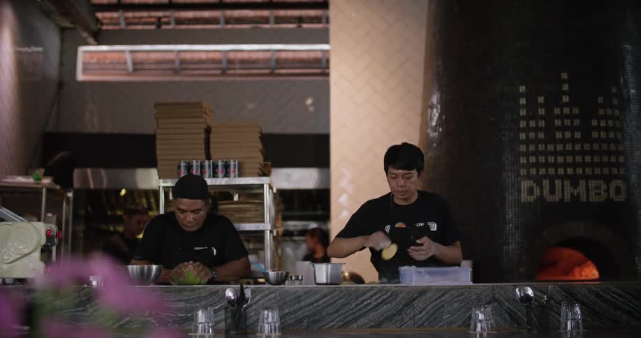 Chefs work at counter with dough with pizza oven and pizza boxes in the background