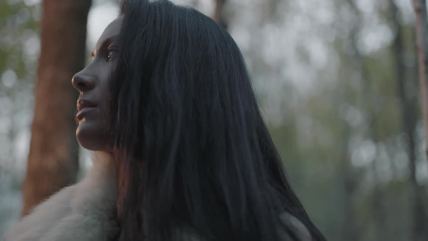 Woman wearing animal fur sitting and staring off in the forest