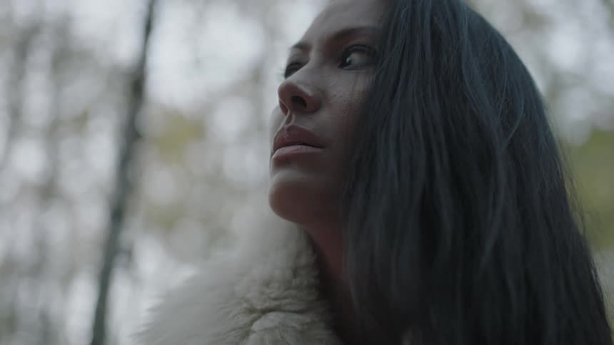 A woman wearing fur looks up on a cloudy day