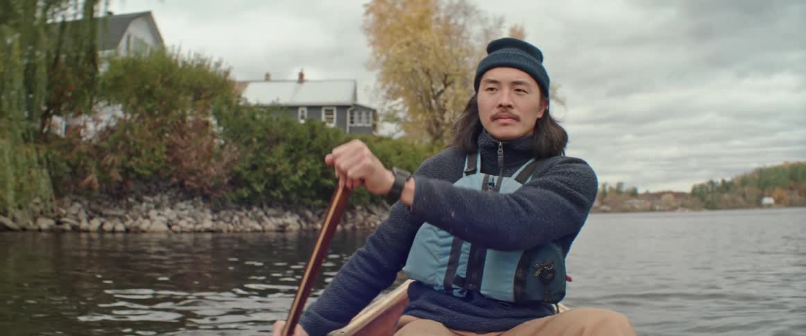 A man wearing warm clothing slowly paddles to turn his canoe in the water