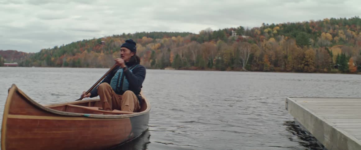 A man pushes off in his canoe on a lake on a cloudy fall day