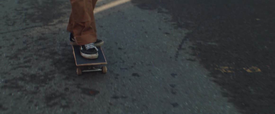 A skateboarder rides his board along a road during at sunrise