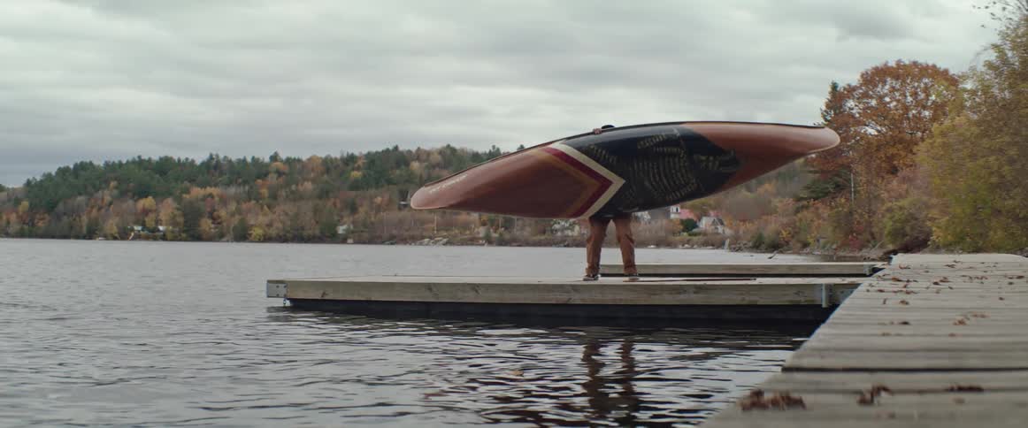 A man carries a canoe on his head to a dock and lays it down