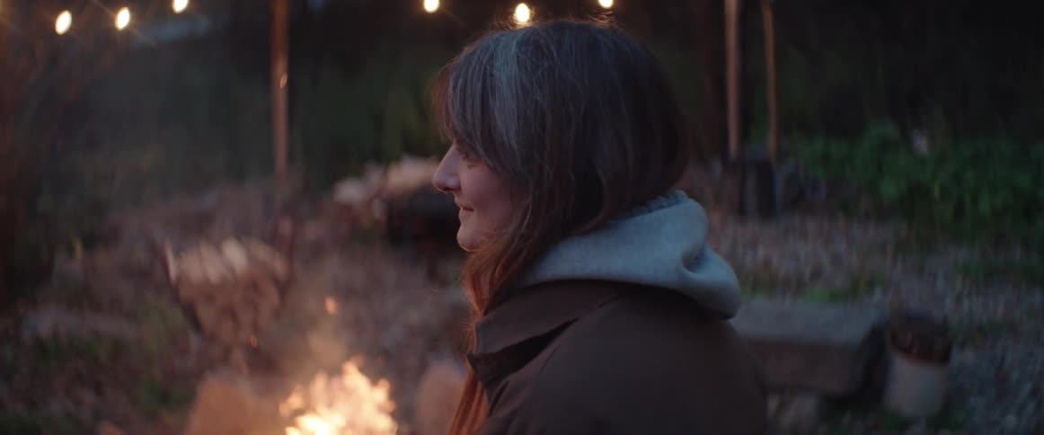 A woman sits by a roaring fire pit in her backyard in the evening