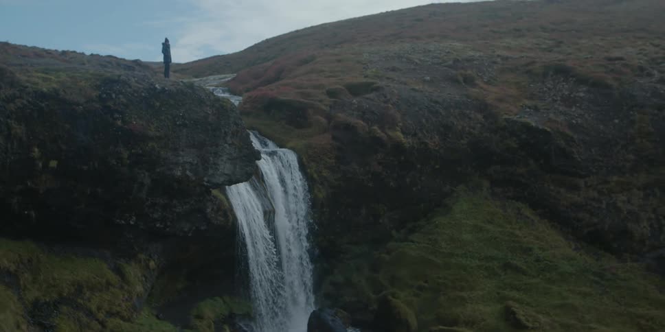 Silhouette of a person standing on top of a mountain as a waterfall flows below