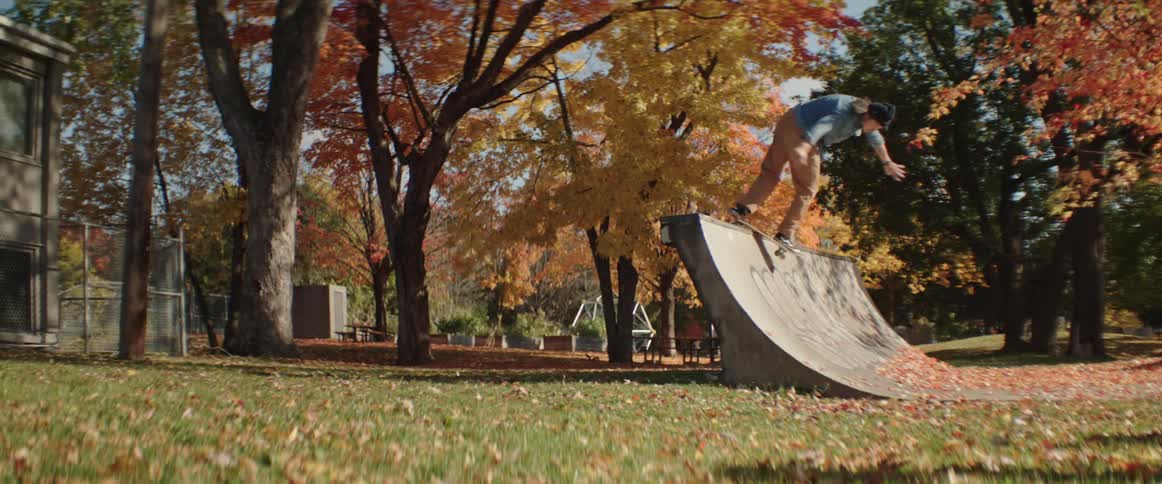 A man performs a lip trick on his skateboard on a ramp under bright fall colored trees