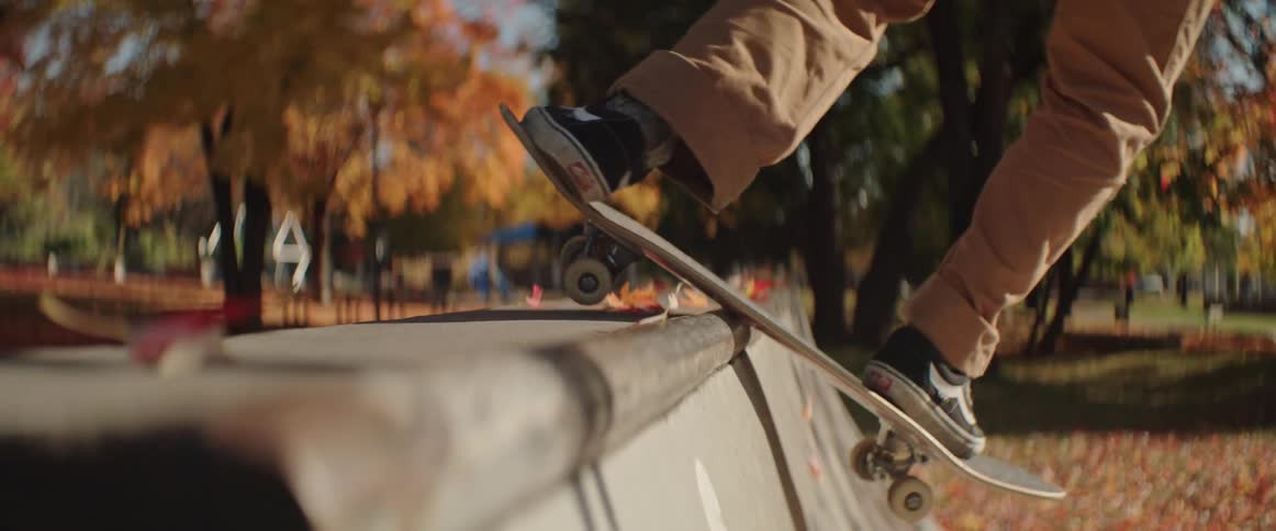 Close up of a man hitting a concrete mini ramp on his skateboard in the park