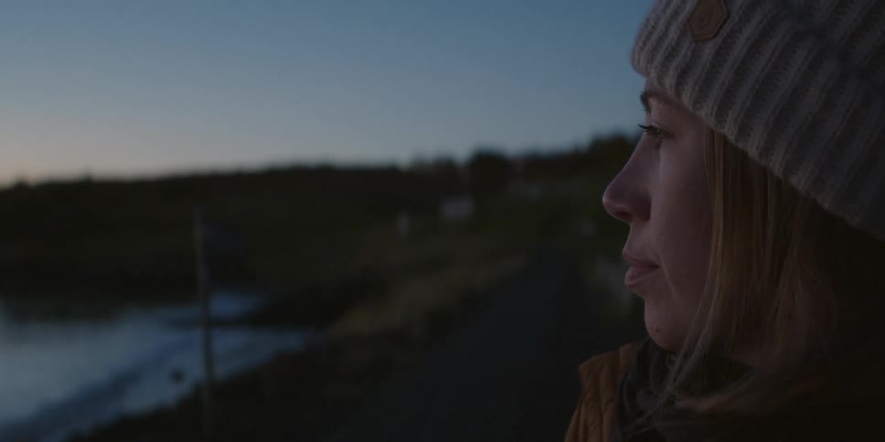A woman stands outside on a cold day while looking out over the water