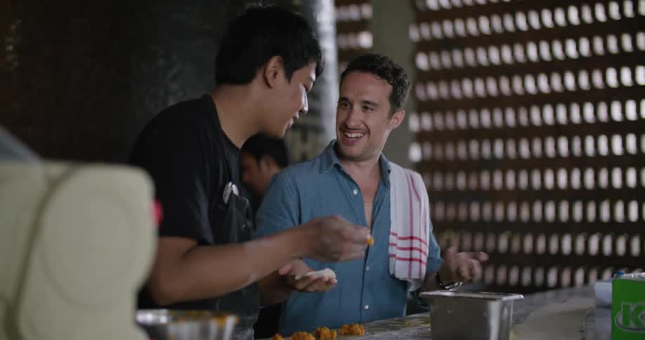 Two men are talking as they work behind a bar and one man is moving his arms and hands as he speaks