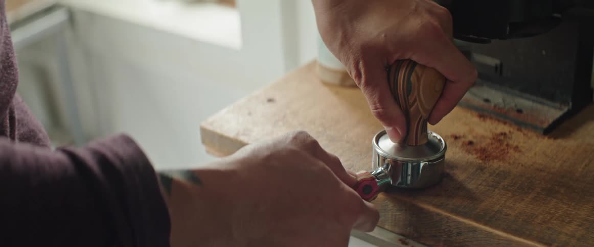 A man tamps coffee grounds by his espresso machine