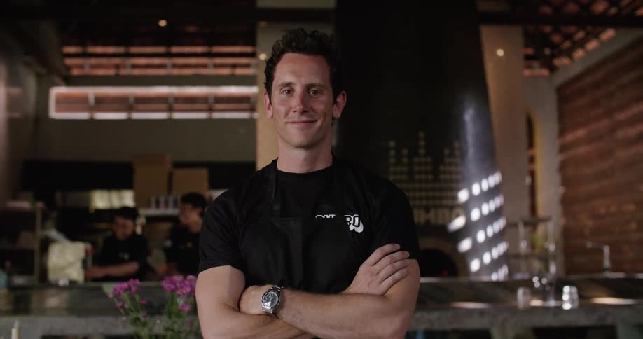 Restaurant boss stands posing while other workers work in kitchen in the background