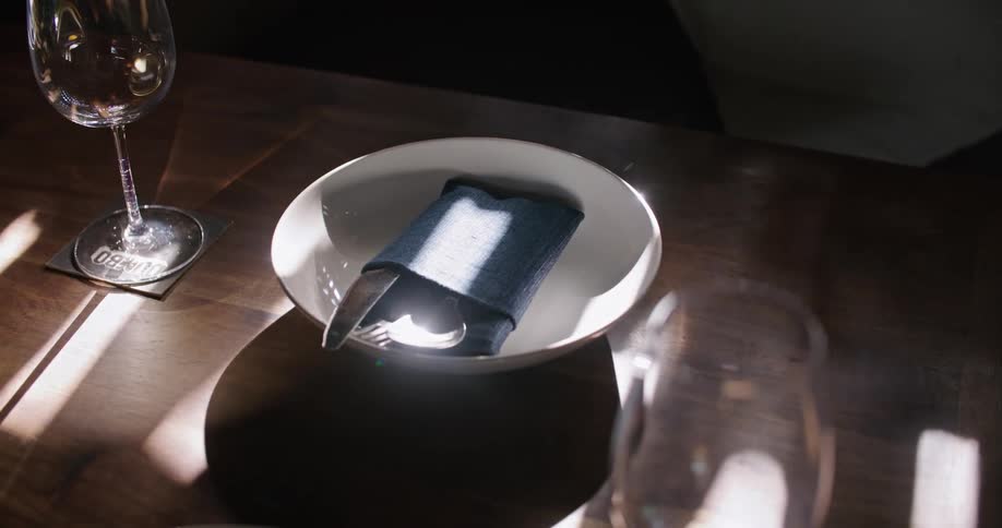 Orbiting footage of cutlery wrapped on a blue napkin inside a dish on a table